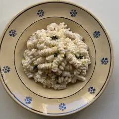 Piatto di pasta ricotta e limone, condita con erbe aromatiche e pepe nero, servita in un piatto di ceramica decorato.