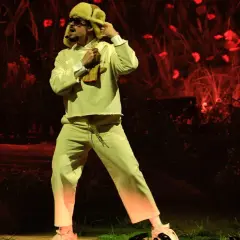 Bad Bunny w beżowym dresie i futrzanej czapce, jakby z "bad bunny café con ron tekst", tańczy na tle czerwonych kwiatów.