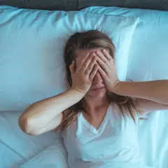 Mujer en la cama, con las manos cubriendo sus ojos. Son las 4 de la mañana y no puedo dormir, la luz azulada ilumina la escena.