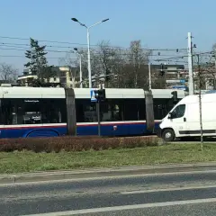 Tramwaj na rondzie, obok biała furgonetka. Czy tramwaj ma pierwszeństwo na rondzie? Znak informuje o ruchu okrężnym.
