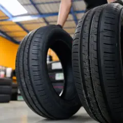 Deux pneus de voiture neufs, une sous-marque Michelin, sont présentés dans un entrepôt rempli de pneus.