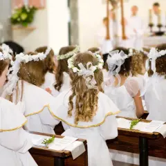 Dziewczynki w bieli, z wiankami na głowach, czekają na uroczystość. Krótkie życzenia na komunię dla nich.