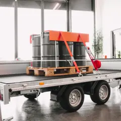 Fass auf einem Anhänger sind drei Fässer auf einer Palette sicher mit roten Gurten und einem orangefarbenen Halter frei verladen.