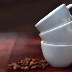 Tre tazzine bianche impilate e chicchi di caffè. Una tazzina di caffè contiene circa 60 ml.