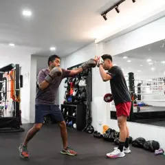 Two men train in a boxing gym. One throws a punch, the other blocks, showcasing resilient boxing.
