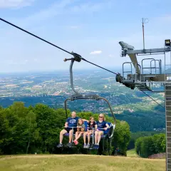 Rodzina na wyciągu krzesełkowym podziwia panoramę Wisły i okolicznych gór.