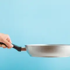 Dłoń trzyma aluminiową patelnię. Czy patelnia aluminiowa jest zdrowa? To pytanie nurtuje wielu kucharzy.