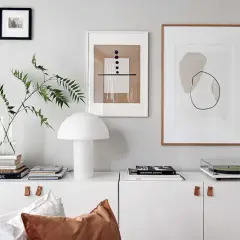 En vit skåp med en lampa, böcker, en skivspelare och tre tavlor utan ramar på väggen.