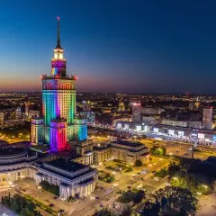 Pałac Kultury i Nauki w Warszawie, o imponującej wysokości, rozświetlony tęczowymi barwami na tle nocnego nieba.