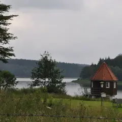 Kleines Holzhaus mit Spitzdach am Seeufer, ideal für einen Spaziergang auf dem kerspetalsperre rundweg.