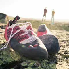 Kletterschuhe ruhen auf moosbewachsenem Fels. Im Hintergrund stehen zwei Kletterer. Zeit für kletterschuhe waschen.