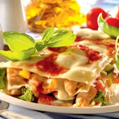 Pyszne lasagne z kurczakiem, brokułami i pomidorami, udekorowane świeżą bazylią.