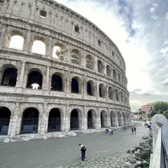Vue extérieure du Colisée, monument emblématique de Rome. Des touristes profitent de leur visite colisée sous un ciel nuageux.