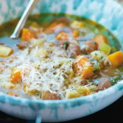 En närbild av en skål med en mustig gryta, kanske ett molokhia recept, med bitar av grönsaker och kött, toppad med riven ost.