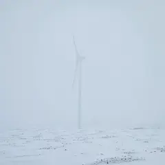 Wiatr huczy jak wiersze o smutku i żalu. Samotna turbina na zaśnieżonym polu, w mglistym, przygnębiającym krajobrazie.