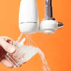 Un robinet avec un filtre blanc verse de l'eau dans un verre. C'est le moment de changer le filtre robinet pour une eau plus pure.