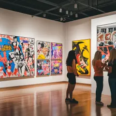 Three women admire a collection of vibrant, famous pop art in a gallery.