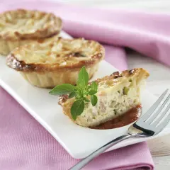 Trois mini quiches sans pâte garnies d'une tranche coupée, sur une assiette blanche avec une feuille de basilic.