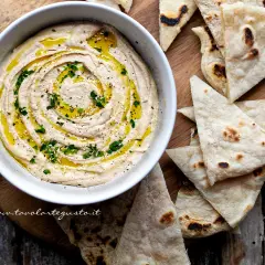 Cremoso hummus di fagioli, condito con olio d'oliva e prezzemolo, servito con pane pita tostato.