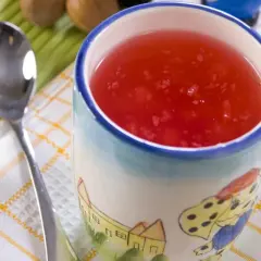 Czerwony kisiel w kubeczku z bajkowym wzorem, obok łyżeczka. Kisiel jest dobry na trawienie i lekkostrawny.