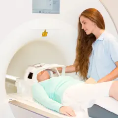 Pacjentka leży w aparacie do rezonansu magnetycznego, przygotowując się do tomografii głowy. Technik medyczny czuwa nad przebiegiem badania.