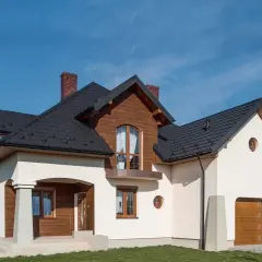 Nowy dom z drewnianymi elementami i białym tynkiem. Co to jest cokół? To ta jasna, kamienna podstawa, która chroni ściany przed wilgociącią.