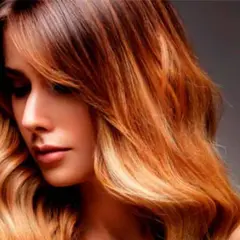 Mujer con pelo californianas, con ondas y un degradado de color castaño a rubio dorado, luciendo un estilo moderno y radiante.