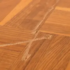 Gros plan sur un parquet en bois avec une rayure profonde et des éclats, témoignant d'une usure du temps.