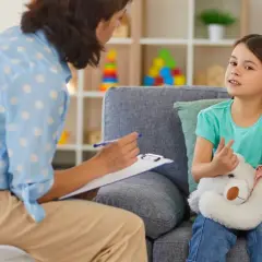 Dziecko z pluszowym misiem rozmawia z psychologiem dziecięcym.