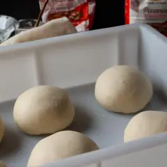 Mehrere Teigkugeln liegen in einer weißen Box, bereit für das Pizzateig einfrieren. Im Hintergrund sind Zutaten und eine Pizzatüte zu sehen.