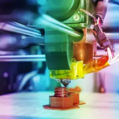 Głowica drukarki 3D drukuje brązową śrubę na platformie roboczej.