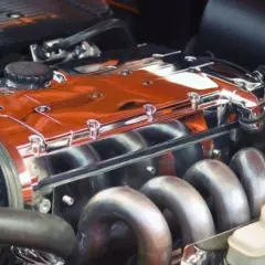 Motore lucido con collettori cromati e coperchio arancione brillante. Sembra un motore fuso, pronto per essere installato.