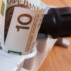 Zrolowany banknot 10 zł w gniazdku listwy zasilającej symbolizuje sposoby na oszczędzanie prądu i pieniędzy.