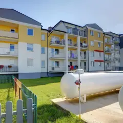 Nowoczesny blok z kolorową elewacją i balkonami. Obok plac zabaw i duże zbiorniki, które zapewniają ogrzewanie gazowe w bloku.