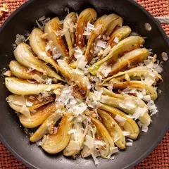 Finoçchi gratinati in padella, dorati e saporiti, guarniti con scaglie di formaggio e noci croccanti.