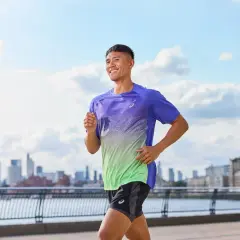 Uśmiechnięty mężczyzna w sportowym stroju biegnie nad rzeką, z panoramą miasta w tle. Czy warto biegać? Ten widok mówi wszystko!