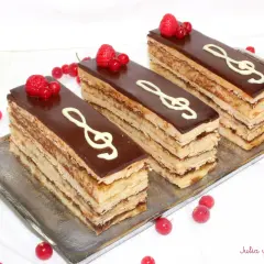 Tres porciones de pastel ópera, con capas de bizcocho y crema, cubiertas de chocolate y decoradas con clave de sol y frutos rojos.