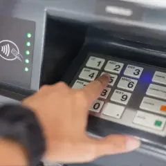 Une main tape un code sur un clavier de distributeur. Comment retrouver son code de carte bancaire ? La sécurité avant tout.