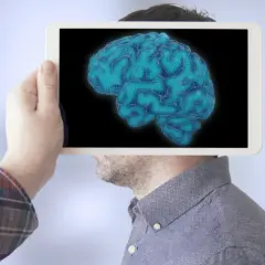 Dłoń trzyma tablet z cyfrowym mózgiem, sugerując analizę poziomów IQ.