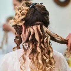 Fryzury z długich włosów na wesele: loki i doczepiane pasma tworzą objętość i blask. Stylista dopracowuje detale.