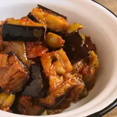 Caponata que es: un delicioso guiso siciliano de berenjenas, aceitunas y tomate, servido en un cuenco blanco.