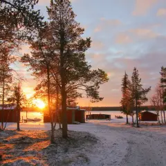 Solnedgång över camp alta kiruna. Röda stugor och snö täcker marken.