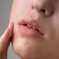 Labios rosados y brillantes, con una textura que podría sugerir la presencia de hongos en los labios, tocados suavemente por un dedo.