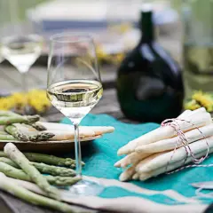Ein Glas Weißwein steht neben frischem Spargel auf einem Holztisch. Perfekt für den Genuss von Wein zum Spargel.