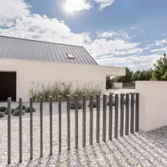 Nowoczesny dom z białym tynkiem i szarym dachem. Przed nim minimalistyczne, metalowe ogrodzenie.