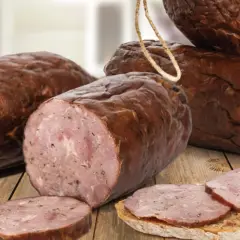 Kiełbasa żywiecka, wędzona, z widocznym przekrojem i plastrami na chlebie, prezentuje się apetycznie na drewnianym stole.