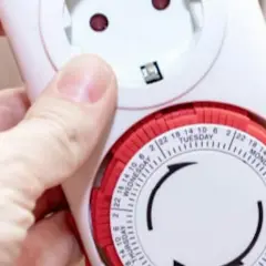 Dłoń trzyma mechaniczny zegar czasowy z tarczą dni tygodnia i godzin. Dowiedz się, jak ustawić zegar czasowy, aby zaplanować włączanie i wyłączanie urządzeń.
