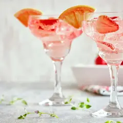 Orzeźwiające drinki z truskawkami i plasterkami grejpfruta, idealne na letnie popołudnie. W tle widać świeże truskawki.