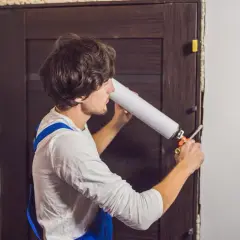 Un homme utilise une mousse expansive pour comment isoler une porte. Il applique le produit dans l'encadrement.