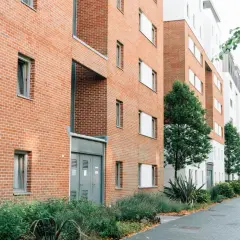 Nowoczesny budynek mieszkalny z cegły i białego tynku, z zielenią przed wejściem.